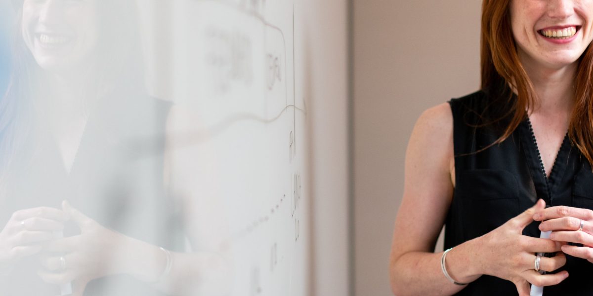 A business professional actively outlining a step-by-step investment strategy on a whiteboard during a planning session.